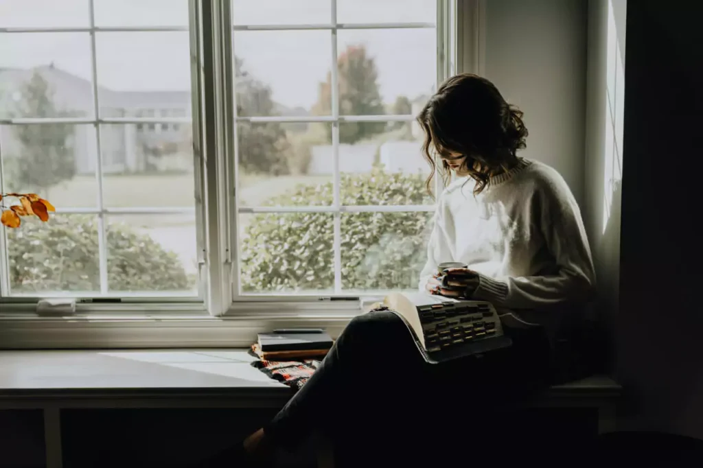 An introverted woman next to window reading
