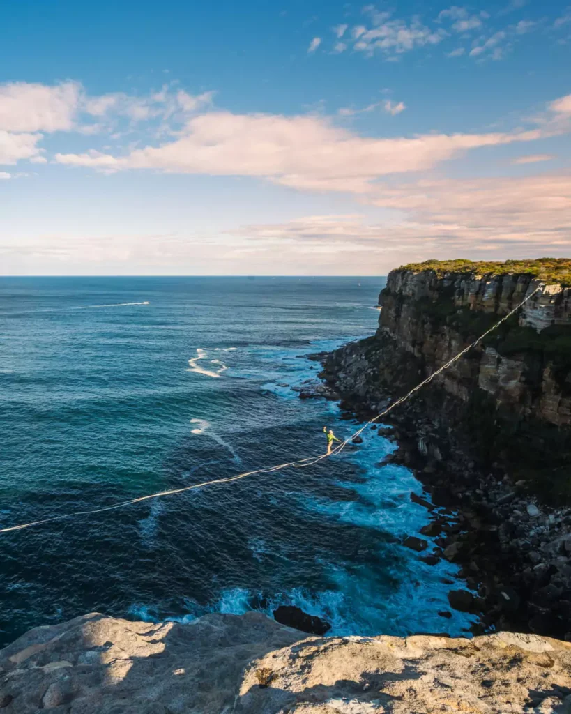 Person walking on a tightrope over ocean cliffs symbolizing courage and calculated risks