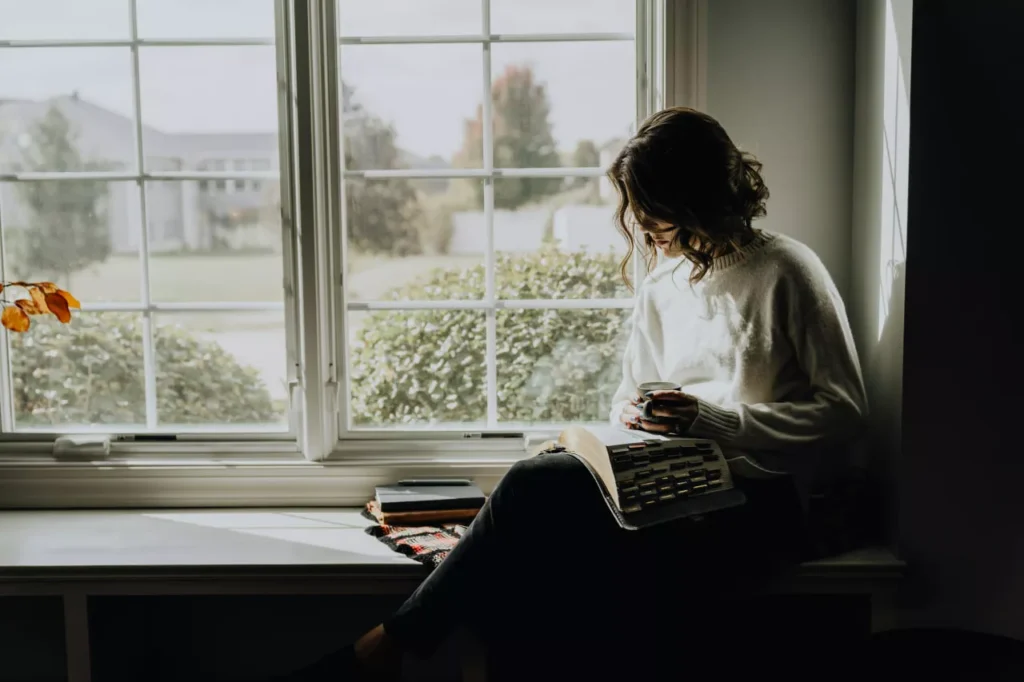 A woman in solitude reading in a nice room by the window